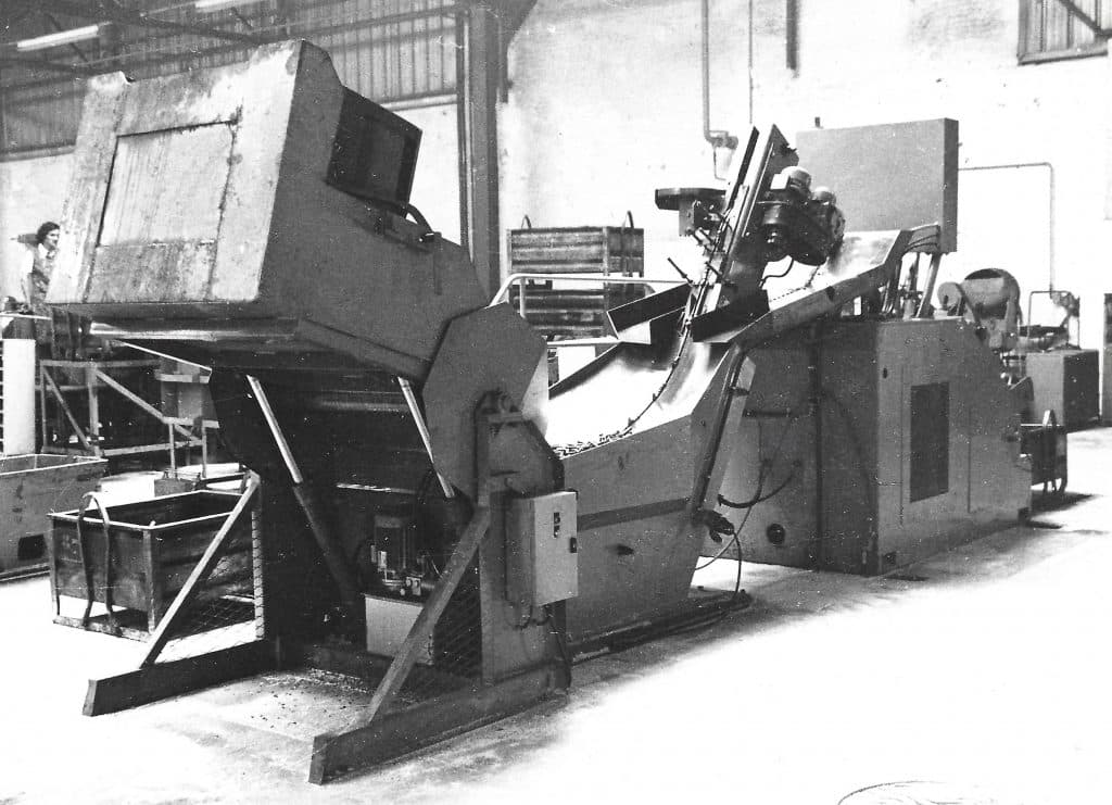 An old mechanical device used to lift and unload steel containers within a factory, reflecting Manergo's roots in material handling.