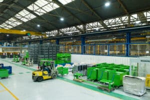 Vue générale de l'atelier de production Manergo, montrant un chariot élévateur circulant au milieu de nombreuses bennes de collecte vertes et de bacs de stockage.