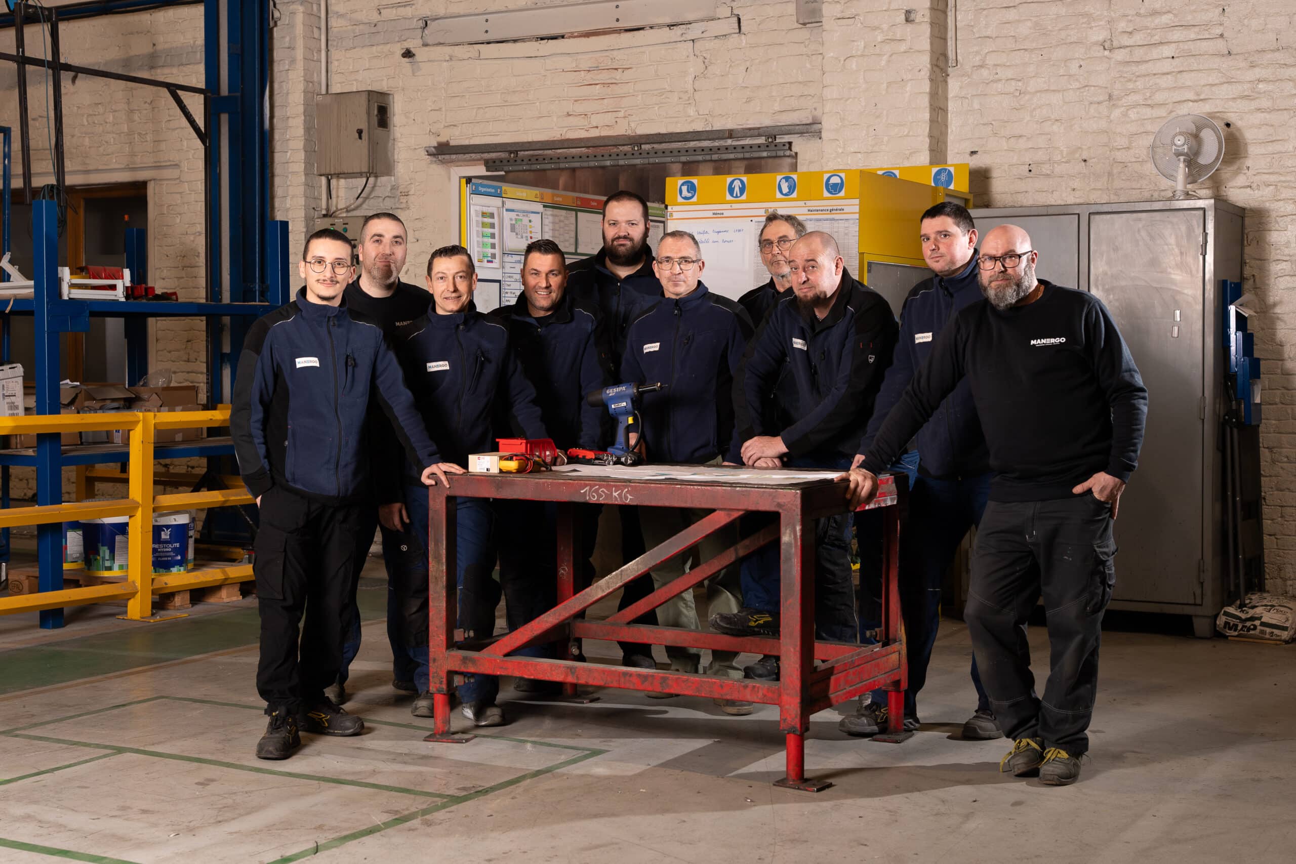 Une dizaine d'opérateurs et techniciens de l'équipe de production Manergo, réunis en tenue de travail autour d'un établi en métal dans l'atelier.